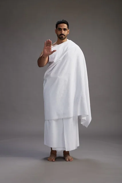 بورتريه لرجل عربي سعودي خليجي يرتدي ملابس الإحرام لأداء مناسك الحج, العباده والتقرب الى الله , الحج والعمره في مكه, الجسم بالطول الكامل , خلفيه رماديه