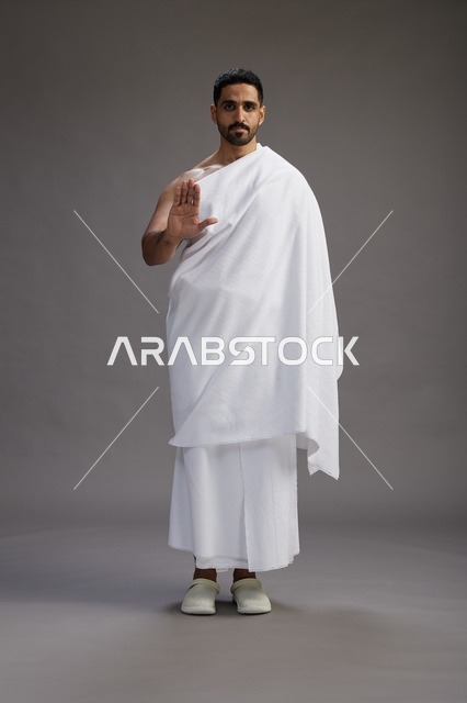 بورتريه لرجل عربي سعودي خليجي يرتدي ملابس الإحرام لأداء مناسك الحج, العباده والتقرب الى الله , الحج والعمره في مكه, الجسم بالطول الكامل , خلفيه رماديه