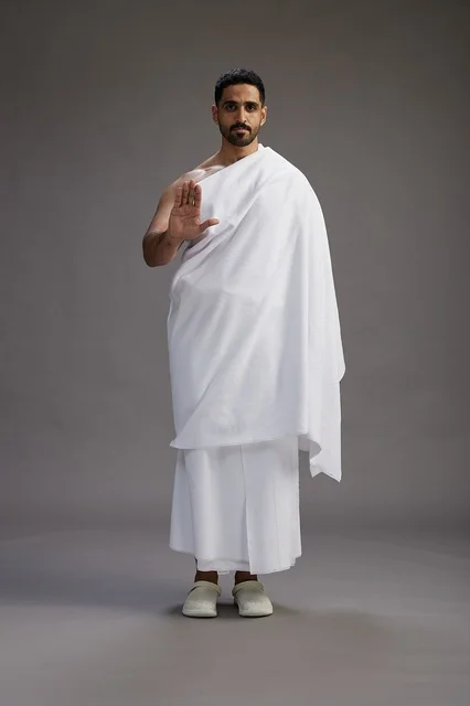بورتريه لرجل عربي سعودي خليجي يرتدي ملابس الإحرام لأداء مناسك الحج, العباده والتقرب الى الله , الحج والعمره في مكه, الجسم بالطول الكامل , خلفيه رماديه