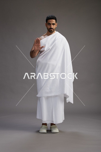 بورتريه لرجل عربي سعودي خليجي يرتدي ملابس الإحرام لأداء مناسك الحج, العباده والتقرب الى الله , الحج والعمره في مكه, الجسم بالطول الكامل , خلفيه رماديه