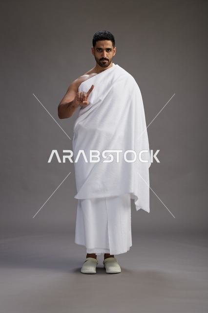 بورتريه لرجل عربي سعودي خليجي يرتدي ملابس الإحرام لأداء مناسك الحج, العباده والتقرب الى الله , الحج والعمره في مكه, الجسم بالطول الكامل , خلفيه رماديه