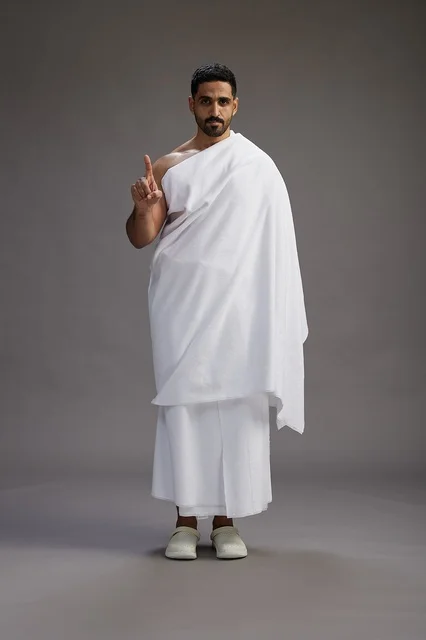 بورتريه لرجل عربي سعودي خليجي يرتدي ملابس الإحرام لأداء مناسك الحج, العباده والتقرب الى الله , الحج والعمره في مكه, الجسم بالطول الكامل , خلفيه رماديه