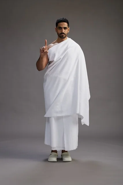 A portrait of an Arab Saudi Gulf man wearing Ihram clothing to perform the rituals of Hajj, worship, and drawing closer to God, Hajj and Umrah in Mecca, full-body, gray background.