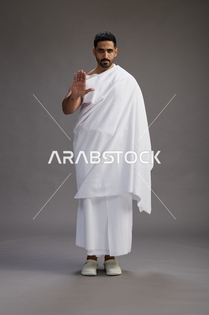 بورتريه لرجل عربي سعودي خليجي يرتدي ملابس الإحرام لأداء مناسك الحج, العباده والتقرب الى الله , الحج والعمره في مكه, الجسم بالطول الكامل , خلفيه رماديه