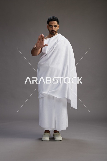 بورتريه لرجل عربي سعودي خليجي يرتدي ملابس الإحرام لأداء مناسك الحج, العباده والتقرب الى الله , الحج والعمره في مكه, الجسم بالطول الكامل , خلفيه رماديه