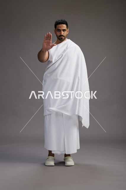 بورتريه لرجل عربي سعودي خليجي يرتدي ملابس الإحرام لأداء مناسك الحج, العباده والتقرب الى الله , الحج والعمره في مكه, الجسم بالطول الكامل , خلفيه رماديه