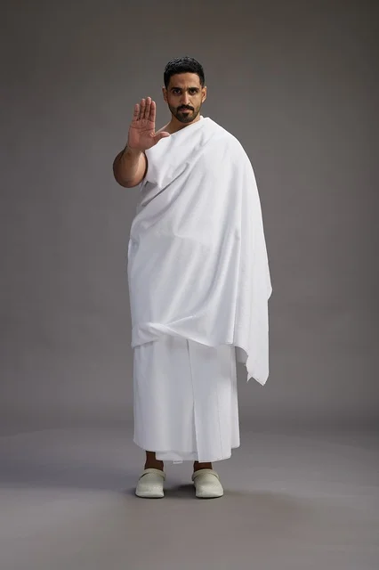 بورتريه لرجل عربي سعودي خليجي يرتدي ملابس الإحرام لأداء مناسك الحج, العباده والتقرب الى الله , الحج والعمره في مكه, الجسم بالطول الكامل , خلفيه رماديه