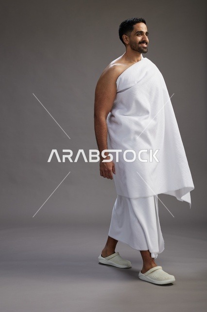 بورتريه لرجل عربي سعودي خليجي يرتدي ملابس الإحرام لأداء مناسك الحج, العباده والتقرب الى الله , الحج والعمره في مكه, الجسم بالطول الكامل , خلفيه رماديه