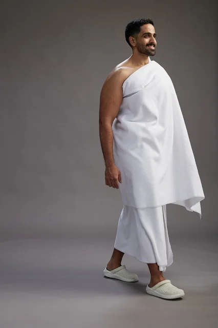 بورتريه لرجل عربي سعودي خليجي يرتدي ملابس الإحرام لأداء مناسك الحج, العباده والتقرب الى الله , الحج والعمره في مكه, الجسم بالطول الكامل , خلفيه رماديه