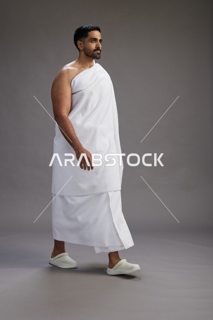 بورتريه لرجل عربي سعودي خليجي يرتدي ملابس الإحرام لأداء مناسك الحج, العباده والتقرب الى الله , الحج والعمره في مكه, الجسم بالطول الكامل , خلفيه رماديه