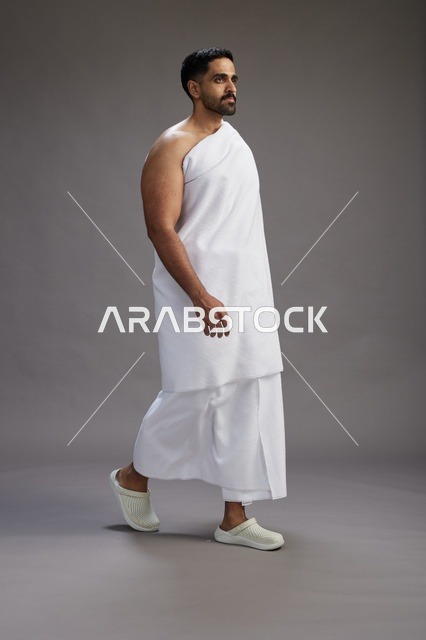 بورتريه لرجل عربي سعودي خليجي يرتدي ملابس الإحرام لأداء مناسك الحج, العباده والتقرب الى الله , الحج والعمره في مكه, الجسم بالطول الكامل , خلفيه رماديه