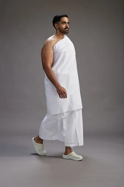 A portrait of an Arab Saudi Gulf man wearing Ihram clothing to perform the rituals of Hajj, worship, and drawing closer to God, Hajj and Umrah in Mecca, full-body, gray background.