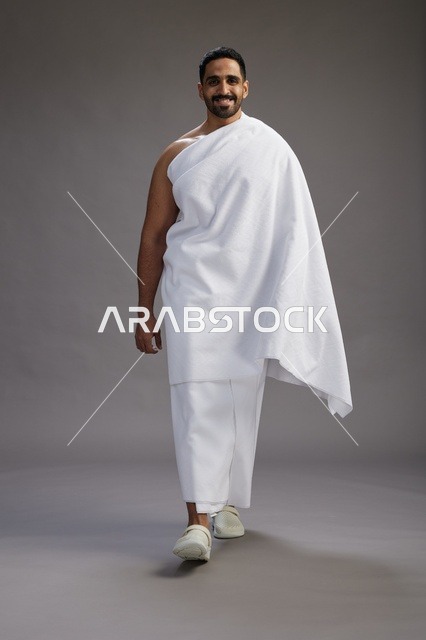 بورتريه لرجل عربي سعودي خليجي يرتدي ملابس الإحرام لأداء مناسك الحج, العباده والتقرب الى الله , الحج والعمره في مكه, الجسم بالطول الكامل , خلفيه رماديه