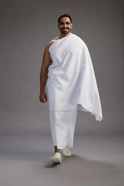 A portrait of an Arab Saudi Gulf man wearing Ihram clothing to perform the rituals of Hajj, worship, and drawing closer to God, Hajj and Umrah in Mecca, full-body, gray background.