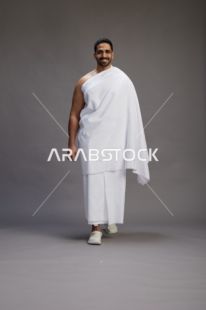 بورتريه لرجل عربي سعودي خليجي يرتدي ملابس الإحرام لأداء مناسك الحج, العباده والتقرب الى الله , الحج والعمره في مكه, الجسم بالطول الكامل , خلفيه رماديه