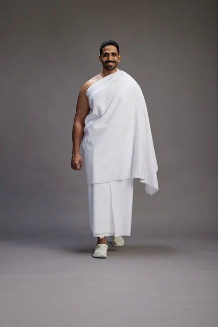 A portrait of an Arab Saudi Gulf man wearing Ihram clothing to perform the rituals of Hajj, worship, and drawing closer to God, Hajj and Umrah in Mecca, full-body, gray background.