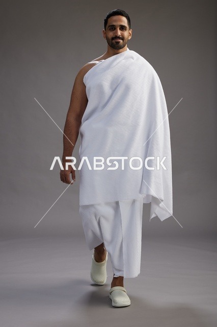 بورتريه لرجل عربي سعودي خليجي يرتدي ملابس الإحرام لأداء مناسك الحج, العباده والتقرب الى الله , الحج والعمره في مكه, الجسم بالطول الكامل , خلفيه رماديه