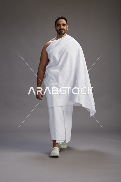 بورتريه لرجل عربي سعودي خليجي يرتدي ملابس الإحرام لأداء مناسك الحج, العباده والتقرب الى الله , الحج والعمره في مكه, الجسم بالطول الكامل , خلفيه رماديه