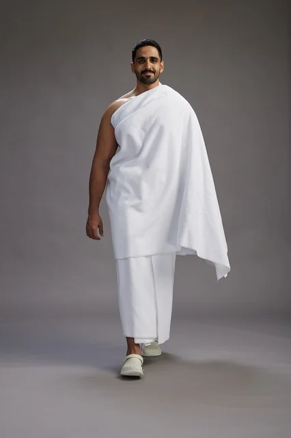 A portrait of an Arab Saudi Gulf man wearing Ihram clothing to perform the rituals of Hajj, worship, and drawing closer to God, Hajj and Umrah in Mecca, full-body, gray background.