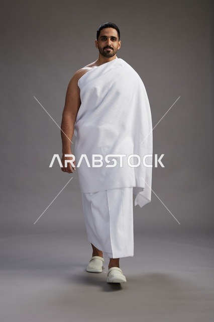 بورتريه لرجل عربي سعودي خليجي يرتدي ملابس الإحرام لأداء مناسك الحج, العباده والتقرب الى الله , الحج والعمره في مكه, الجسم بالطول الكامل , خلفيه رماديه
