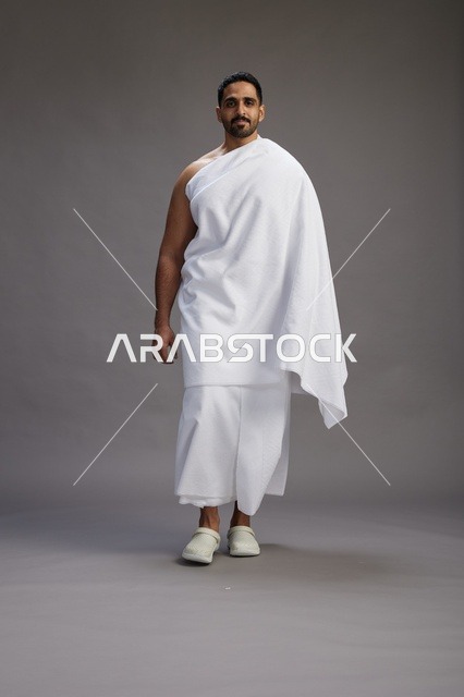 بورتريه لرجل عربي سعودي خليجي يرتدي ملابس الإحرام لأداء مناسك الحج, العباده والتقرب الى الله , الحج والعمره في مكه, الجسم بالطول الكامل , خلفيه رماديه