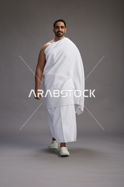بورتريه لرجل عربي سعودي خليجي يرتدي ملابس الإحرام لأداء مناسك الحج, العباده والتقرب الى الله , الحج والعمره في مكه, الجسم بالطول الكامل , خلفيه رماديه