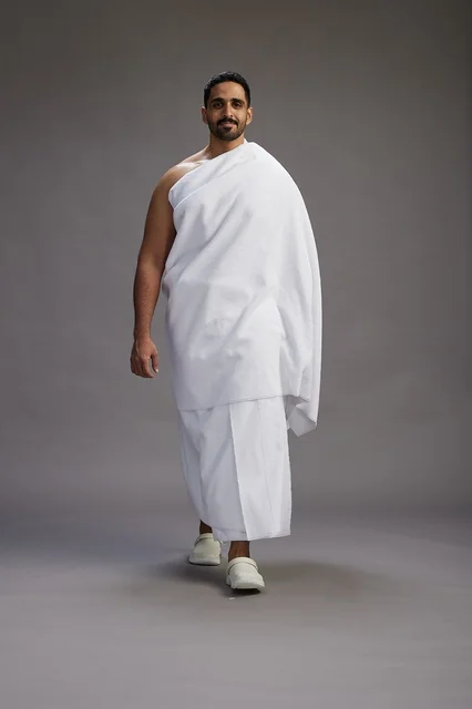 A portrait of an Arab Saudi Gulf man wearing Ihram clothing to perform the rituals of Hajj, worship, and drawing closer to God, Hajj and Umrah in Mecca, full-body, gray background.