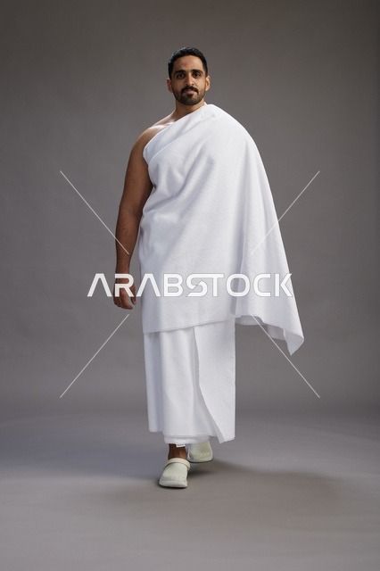 بورتريه لرجل عربي سعودي خليجي يرتدي ملابس الإحرام لأداء مناسك الحج, العباده والتقرب الى الله , الحج والعمره في مكه, الجسم بالطول الكامل , خلفيه رماديه