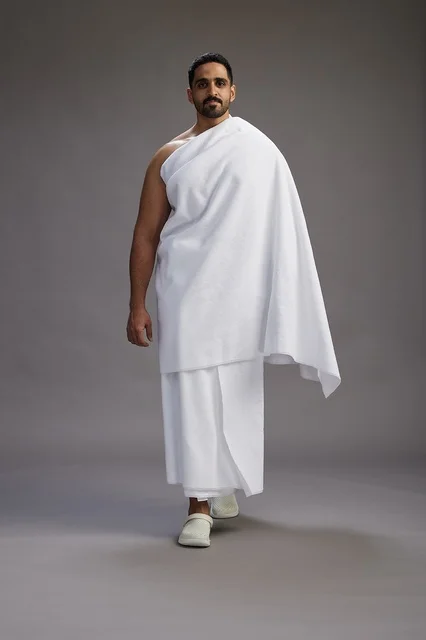 A portrait of an Arab Saudi Gulf man wearing Ihram clothing to perform the rituals of Hajj, worship, and drawing closer to God, Hajj and Umrah in Mecca, full-body, gray background.