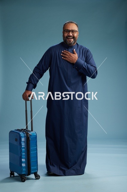 بورتيه لرجل  عربي سعودي  خليجي بثوب أزرق واقف مع حقيبة سفر, الاستعداد للسفر  والسياحه, الجسم بالطول الكامل, خلفيه زرقاء