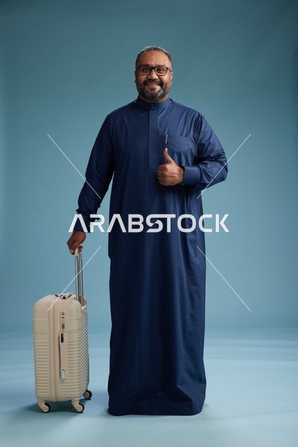 بورتيه لرجل  عربي سعودي  خليجي بثوب أزرق واقف مع حقيبة سفر, الاستعداد للسفر  والسياحه, الجسم بالطول الكامل, خلفيه زرقاء