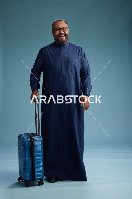 بورتيه لرجل  عربي سعودي  خليجي بثوب أزرق واقف مع حقيبة سفر, الاستعداد للسفر  والسياحه, الجسم بالطول الكامل, خلفيه زرقاء