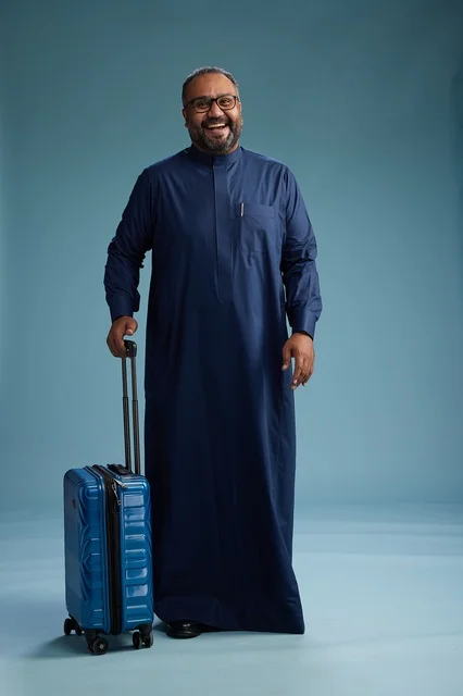 بورتيه لرجل  عربي سعودي  خليجي بثوب أزرق واقف مع حقيبة سفر, الاستعداد للسفر  والسياحه, الجسم بالطول الكامل, خلفيه زرقاء