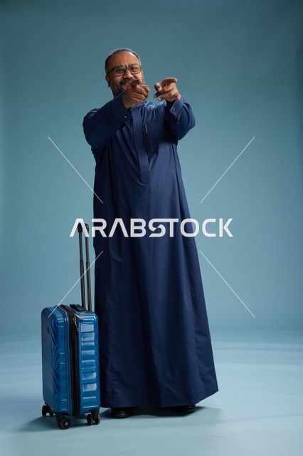 بورتيه لرجل  عربي سعودي  خليجي بثوب أزرق واقف مع حقيبة سفر, الاستعداد للسفر  والسياحه, الجسم بالطول الكامل, خلفيه زرقاء