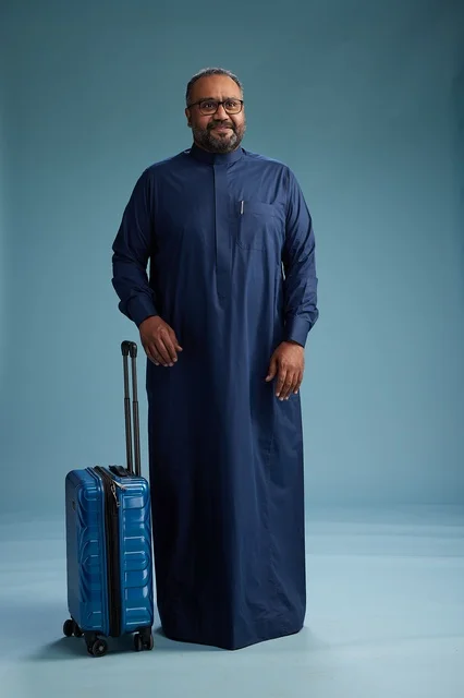 بورتيه لرجل  عربي سعودي  خليجي بثوب أزرق واقف مع حقيبة سفر, الاستعداد للسفر  والسياحه, الجسم بالطول الكامل, خلفيه زرقاء