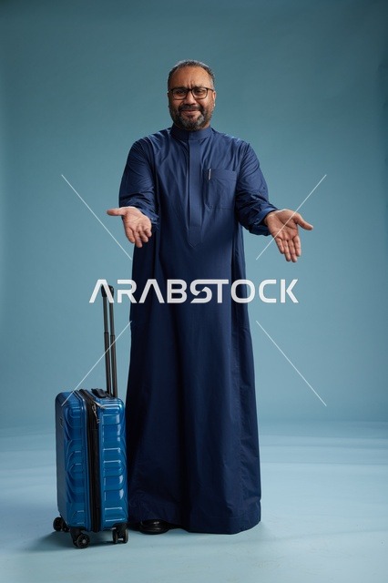 بورتيه لرجل  عربي سعودي  خليجي بثوب أزرق واقف مع حقيبة سفر, الاستعداد للسفر  والسياحه, الجسم بالطول الكامل, خلفيه زرقاء