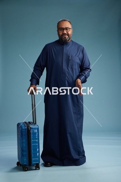 بورتيه لرجل  عربي سعودي  خليجي بثوب أزرق واقف مع حقيبة سفر, الاستعداد للسفر  والسياحه, الجسم بالطول الكامل, خلفيه زرقاء