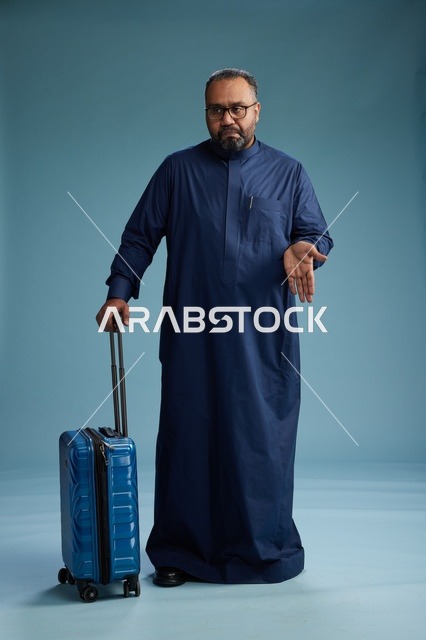 بورتيه لرجل  عربي سعودي  خليجي بثوب أزرق واقف مع حقيبة سفر, الاستعداد للسفر  والسياحه, الجسم بالطول الكامل, خلفيه زرقاء