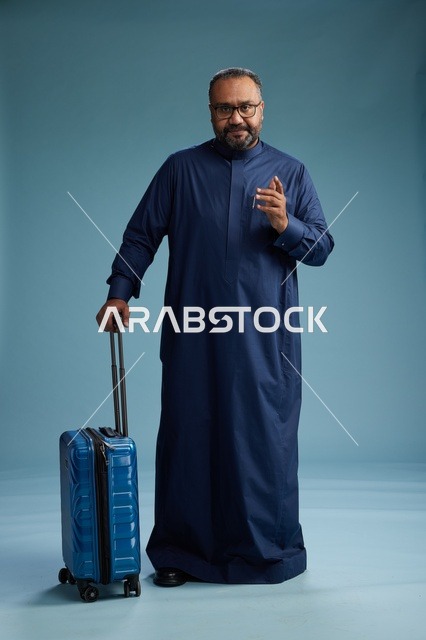 بورتيه لرجل  عربي سعودي  خليجي بثوب أزرق واقف مع حقيبة سفر, الاستعداد للسفر  والسياحه, الجسم بالطول الكامل, خلفيه زرقاء