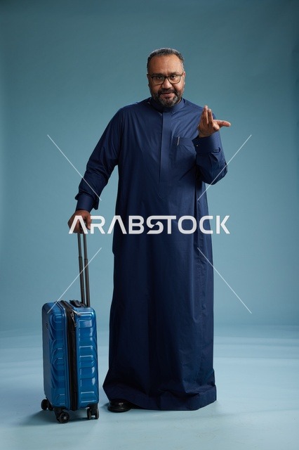 بورتيه لرجل  عربي سعودي  خليجي بثوب أزرق واقف مع حقيبة سفر, الاستعداد للسفر  والسياحه, الجسم بالطول الكامل, خلفيه زرقاء
