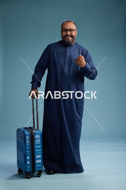 بورتيه لرجل  عربي سعودي  خليجي بثوب أزرق واقف مع حقيبة سفر, الاستعداد للسفر  والسياحه, الجسم بالطول الكامل, خلفيه زرقاء