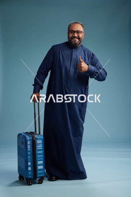 بورتيه لرجل  عربي سعودي  خليجي بثوب أزرق واقف مع حقيبة سفر, الاستعداد للسفر  والسياحه, الجسم بالطول الكامل, خلفيه زرقاء