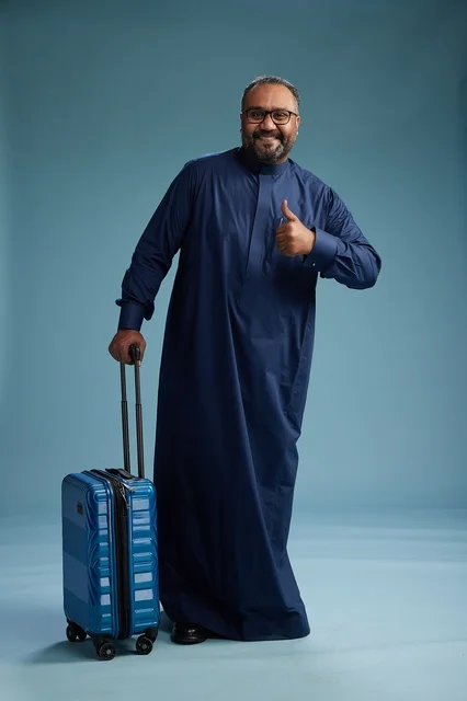بورتيه لرجل  عربي سعودي  خليجي بثوب أزرق واقف مع حقيبة سفر, الاستعداد للسفر  والسياحه, الجسم بالطول الكامل, خلفيه زرقاء