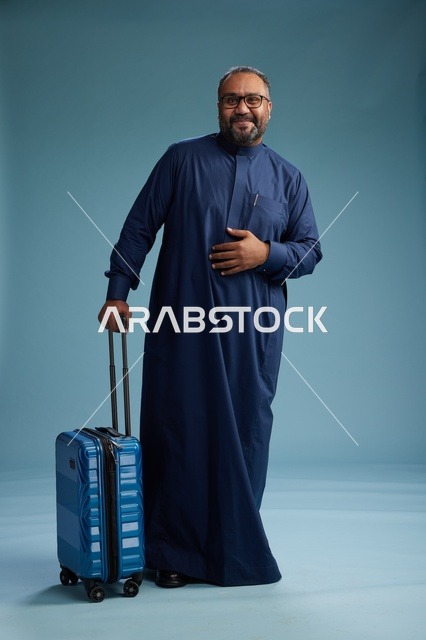 بورتيه لرجل  عربي سعودي  خليجي بثوب أزرق واقف مع حقيبة سفر, الاستعداد للسفر  والسياحه, الجسم بالطول الكامل, خلفيه زرقاء
