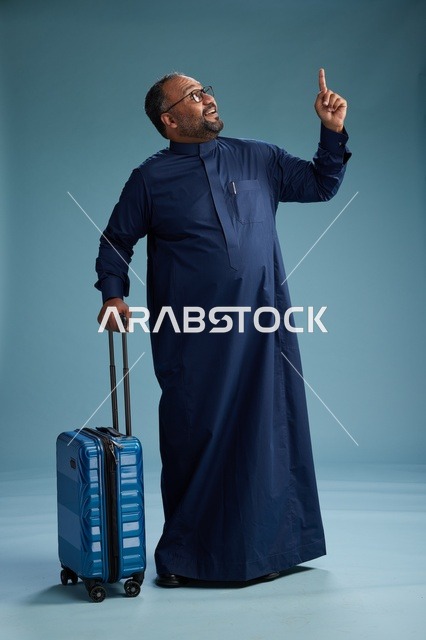 بورتيه لرجل  عربي سعودي  خليجي بثوب أزرق واقف مع حقيبة سفر, الاستعداد للسفر  والسياحه, الجسم بالطول الكامل, خلفيه زرقاء