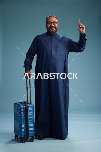 بورتيه لرجل  عربي سعودي  خليجي بثوب أزرق واقف مع حقيبة سفر, الاستعداد للسفر  والسياحه, الجسم بالطول الكامل, خلفيه زرقاء