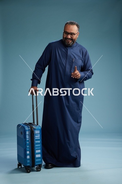بورتيه لرجل  عربي سعودي  خليجي بثوب أزرق واقف مع حقيبة سفر, الاستعداد للسفر  والسياحه, الجسم بالطول الكامل, خلفيه زرقاء