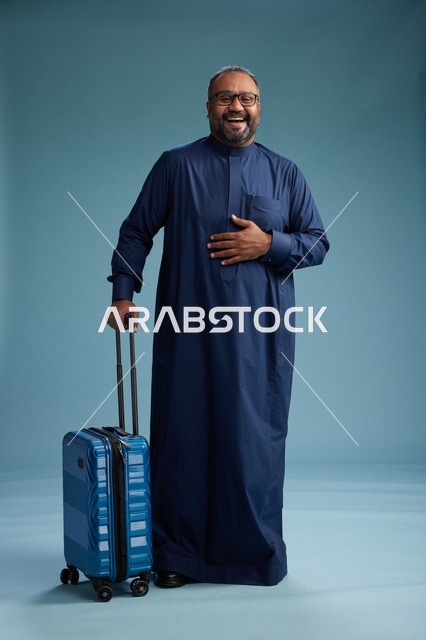 بورتيه لرجل  عربي سعودي  خليجي بثوب أزرق واقف مع حقيبة سفر, الاستعداد للسفر  والسياحه, الجسم بالطول الكامل, خلفيه زرقاء