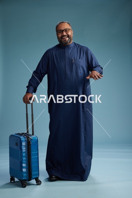 بورتيه لرجل  عربي سعودي  خليجي بثوب أزرق واقف مع حقيبة سفر, الاستعداد للسفر  والسياحه, الجسم بالطول الكامل, خلفيه زرقاء