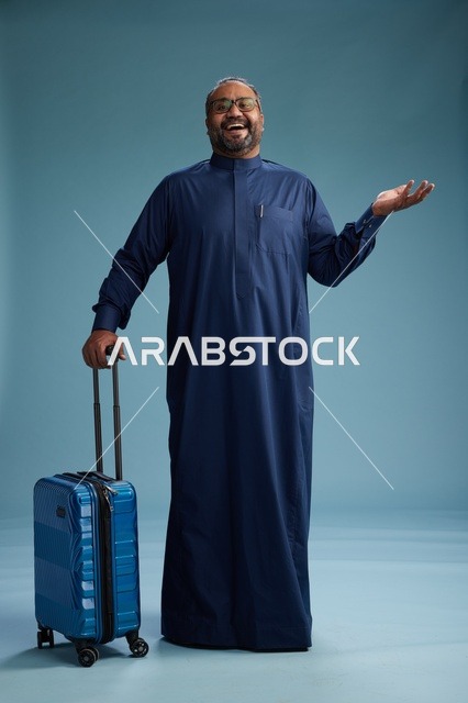 بورتيه لرجل  عربي سعودي  خليجي بثوب أزرق واقف مع حقيبة سفر, الاستعداد للسفر  والسياحه, الجسم بالطول الكامل, خلفيه زرقاء